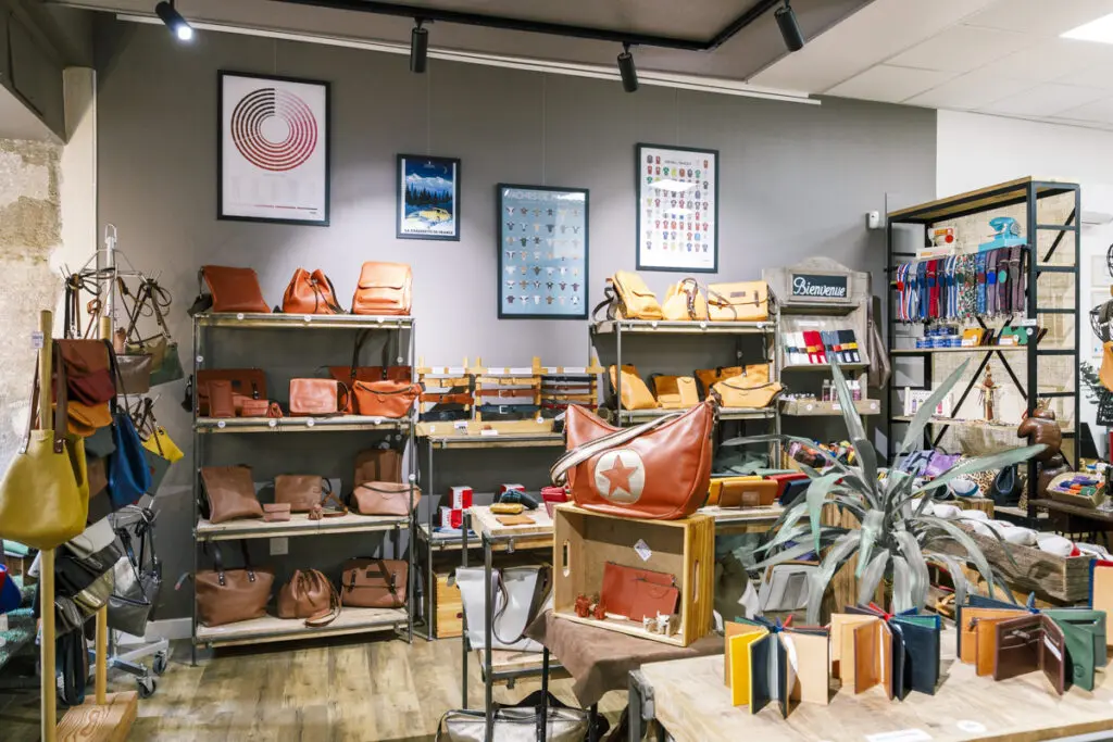Boutique de maroquinerie avec sacs en cuir, portefeuilles colorés et accessoires exposés sur des étagères en bois.