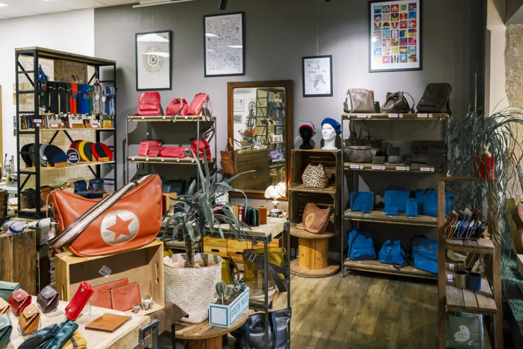 Boutique de maroquinerie colorée avec sacs, portefeuilles et accessoires exposés sur des étagères en bois.